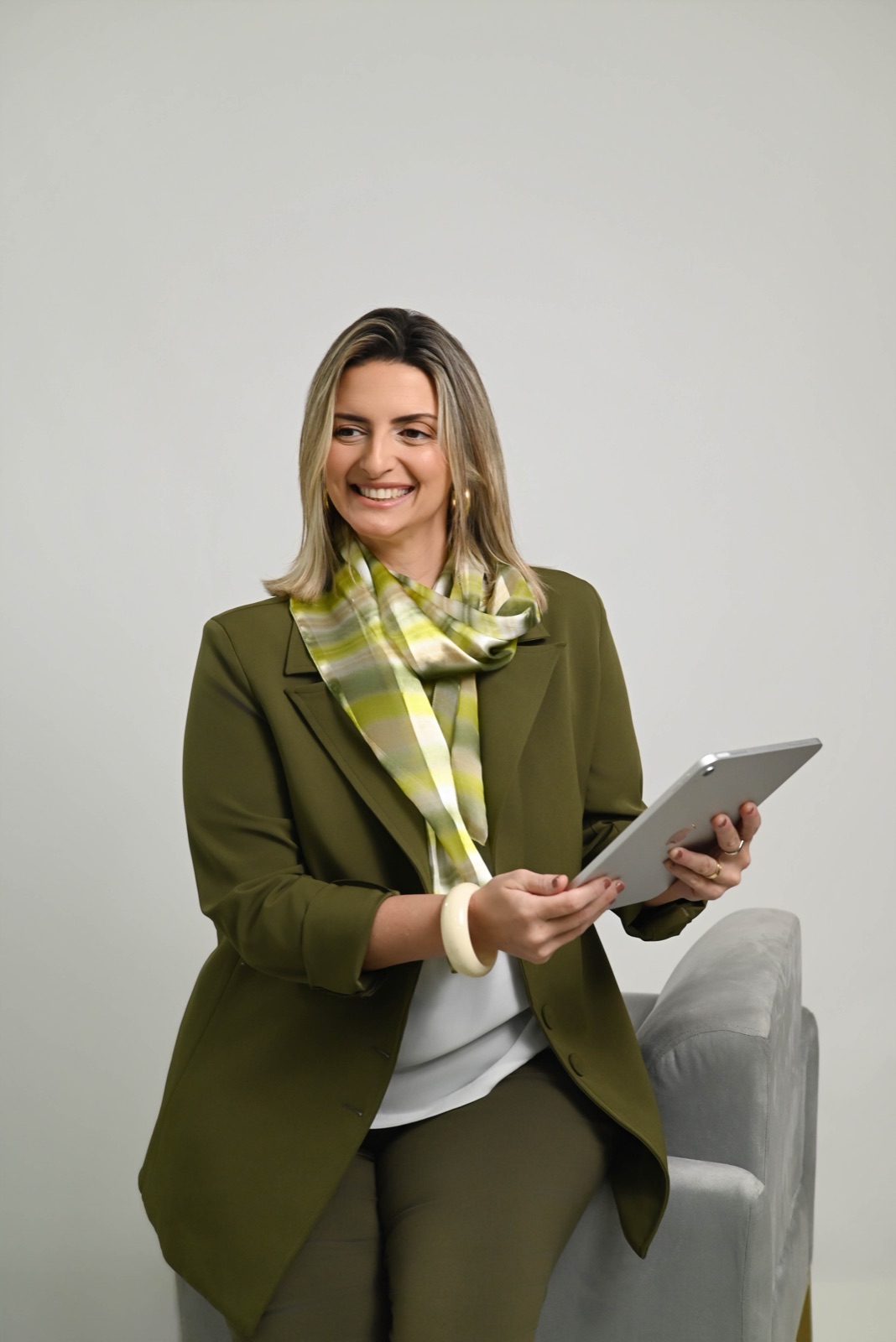 Luiza Palmerini sorrindo com um tablet nas mãos, de blazer verde
