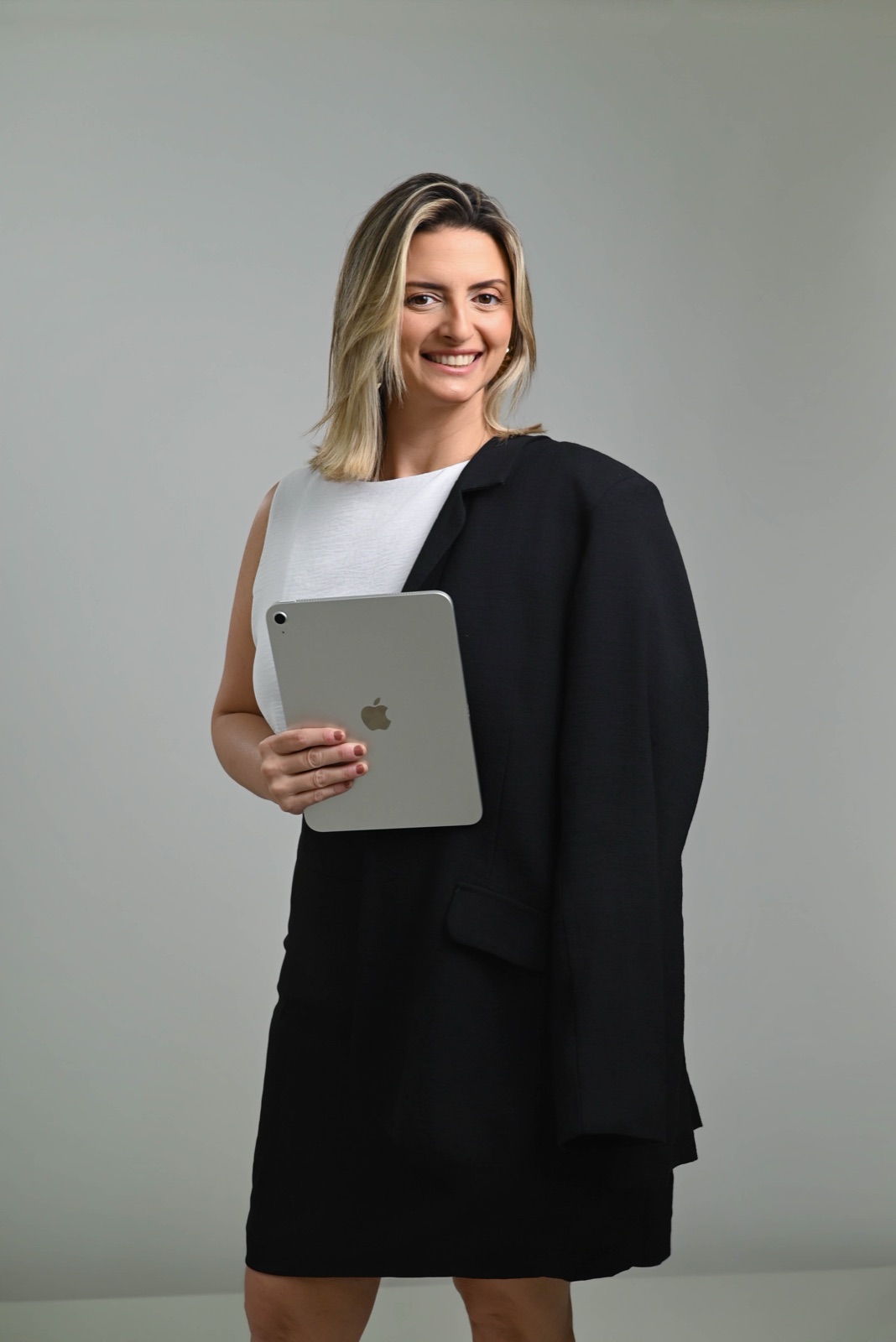 Luiza Palmerini sorrindo, de blazer preto sobre os ombros, segurando um tablet