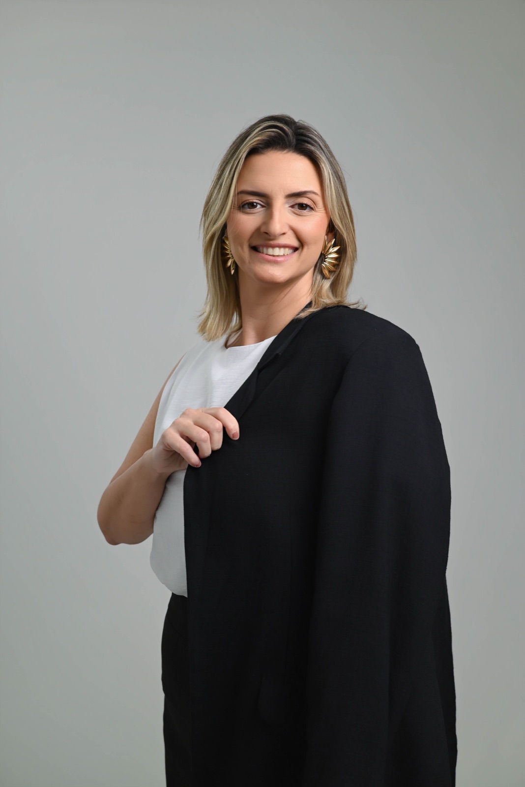 Luiza Palmerini sorrindo, com o blazer preto sobre os ombros